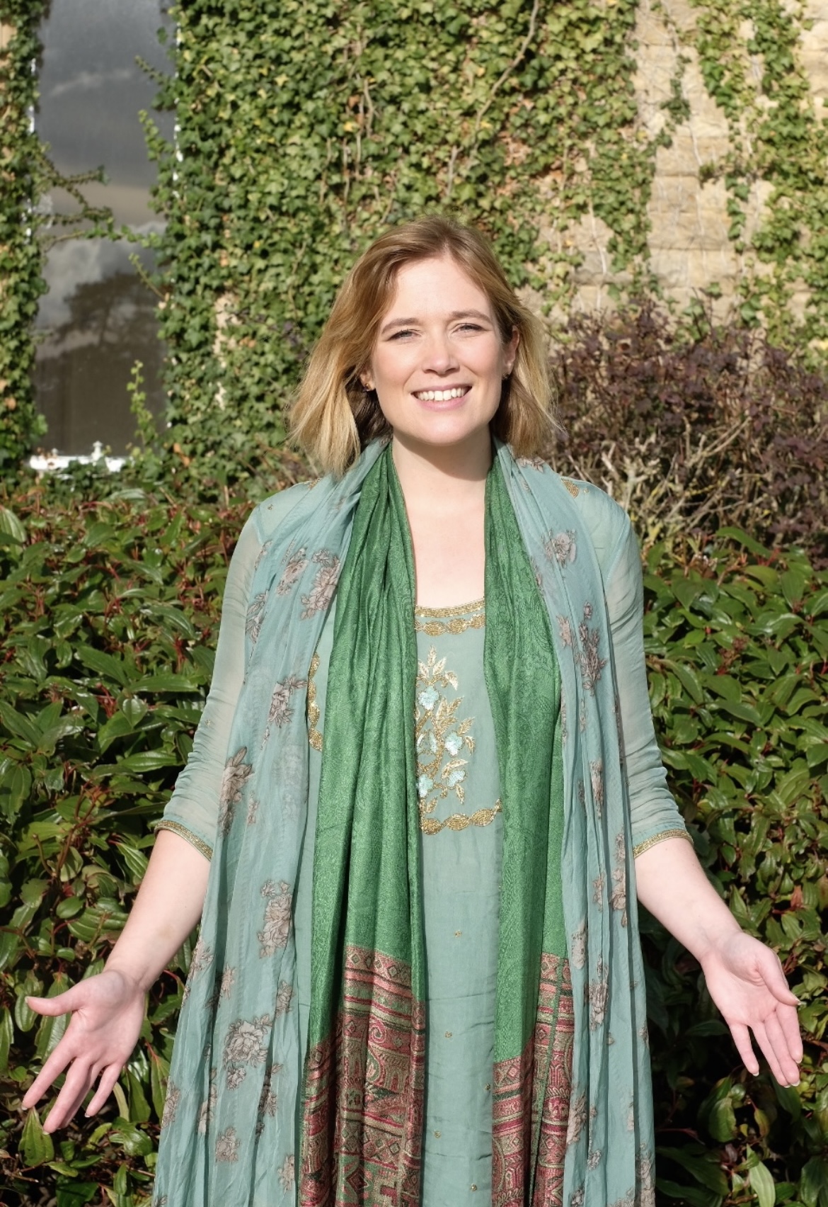 Dr Gayatri Rachel Anderson smiling with open arms in a garden