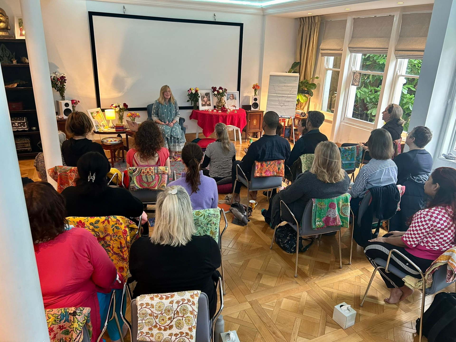 Gayatri leading an in-person Satsang in a flower-filled room