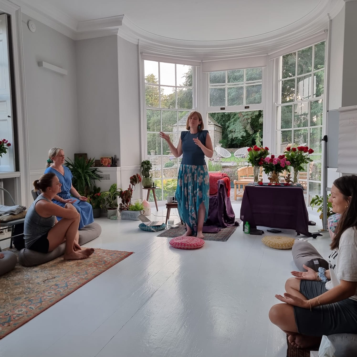 Gayatri guiding a group in meditation in a light-filled room with roses