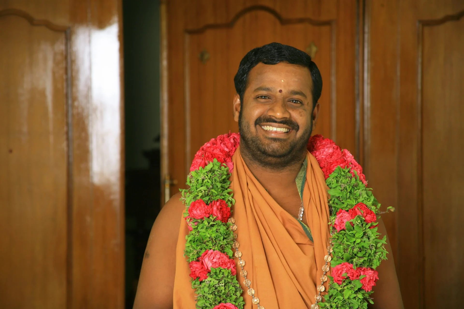 Sri Shakti Amma smiling, adorned with red and green flower garlands